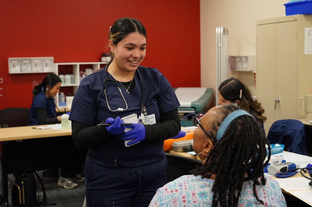 A Certified Medical Assistant instructor has student practice patient history on her.