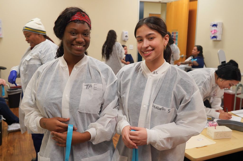 Phlebotomy students smiling in their training lab as they prepare to complete hands-on practice for their phlebotomy certification.